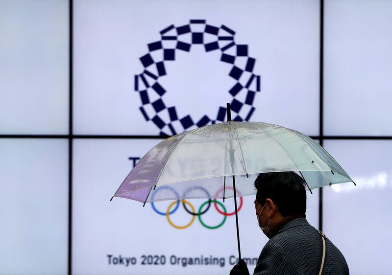 FILE PHOTO: A man wearing a protective face mask walks past in front of a display showing the logo of Tokyo 2020 Olympic Games, amid the coronavirus disease (COVID-19) outbreak in Tokyo