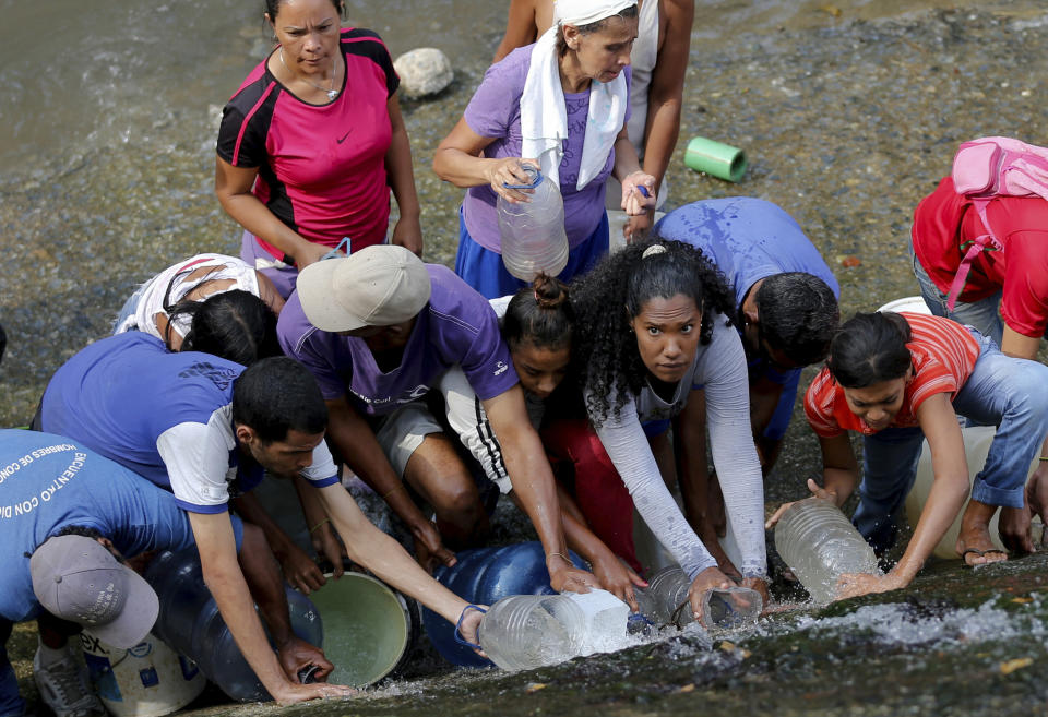 People collect water falling from a leaking pipeline on the bank of the Guaire River during rolling blackouts, which affects access to running water in Caracas, Venezuela, Monday, March 11, 2019. The blackout has intensified the toxic political climate, with opposition leader Juan Guaido blaming alleged government corruption and mismanagement and President Nicolas Maduro accusing his U.S.-backed adversary of sabotaging the national grid. (AP Photo/Fernando Llano)
