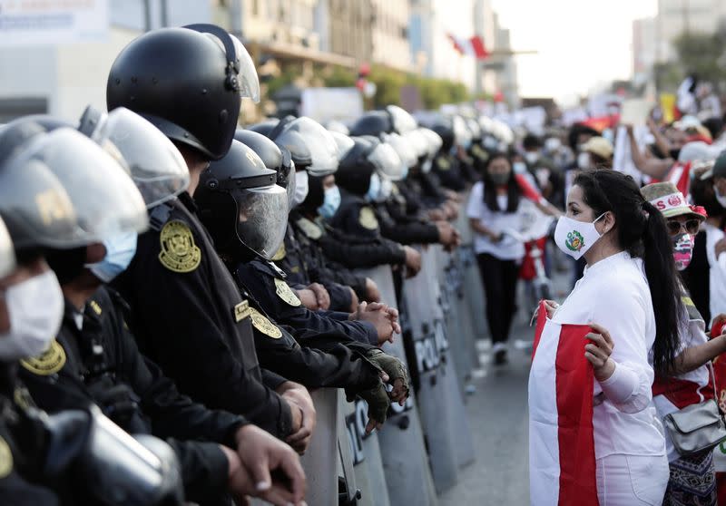 A woman holds a national flag while standing in front of police outside Congress after Peru's interim President Manuel Merino announced his resignation, in Lima