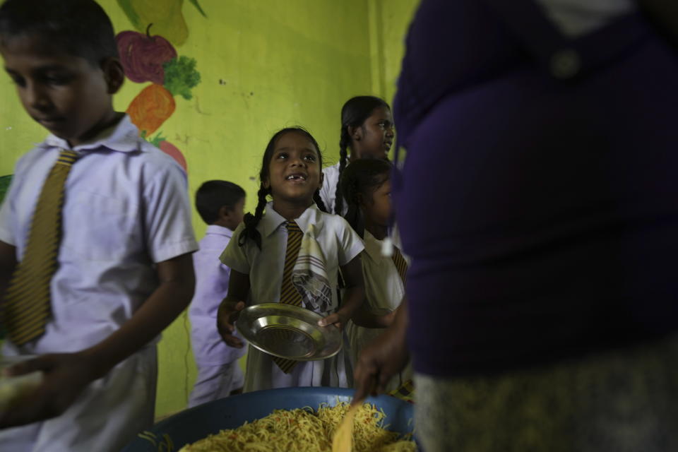 Primary students queue up to receive a free meal given as apart of a feeding program at the Dalukana Primary School in Dimbulagala, about 200 kilometres north east of Colombo, Sri Lanka, Monday, Dec. 12, 2022. (AP Photo/Eranga Jayawardena)