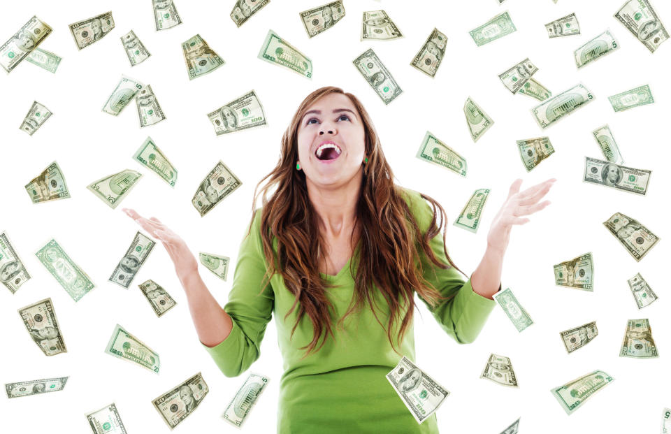 A happy young woman in a green shirt looking up as lots of U.S. currency floats down around her from the sky.