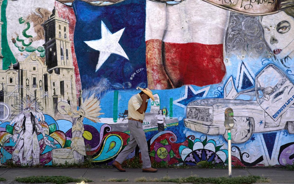 A man adjusts his face mask as he walks past a mural in the heavily Latino section of Oak Cliff in Dallas, Texas.