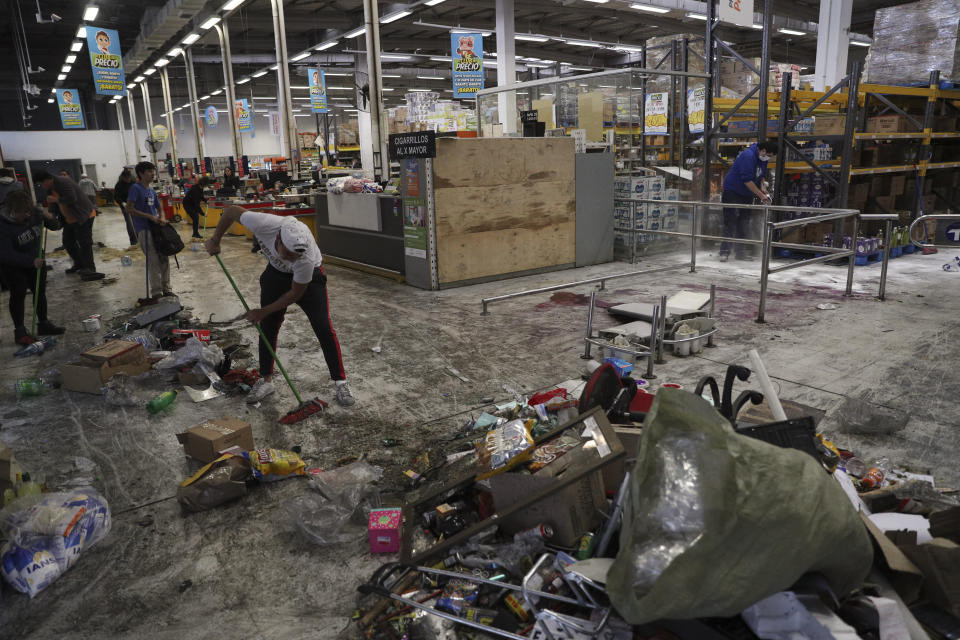 Workers clean up a looted supermarket in Santiago, Chile, Sunday, Oct. 20, 2019. Chilean President Sebastián Piñera on Saturday announced the suspension of a subway fare hike that had prompted violent student protests, less than a day after he declared a state of emergency amid rioting and commuter chaos in the capital. (AP Photo/Esteban Felix)