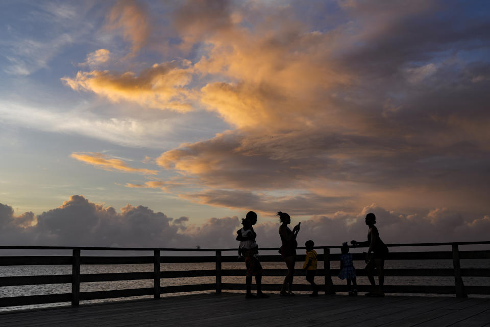 People take photos from the seawall at sunset in Georgetown, Guyana, Wednesday, April 19, 2023. In 2009 Norway signed a deal to provide $250 million in funding to ensure that Guyana's 18 million hectares of forest remain intact. (AP Photo/Matias Delacroix)