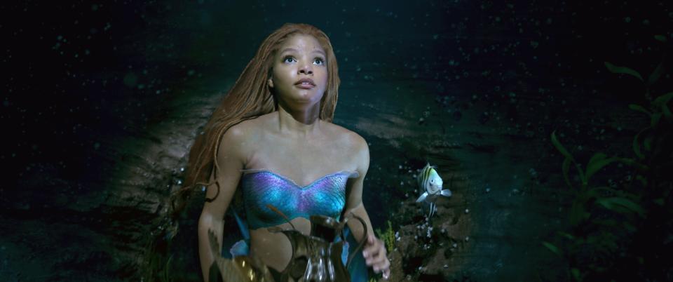 Halle Bailey as Ariel wearing a shimmering mermaid top, looking upward underwater in a scene from "The Little Mermaid"