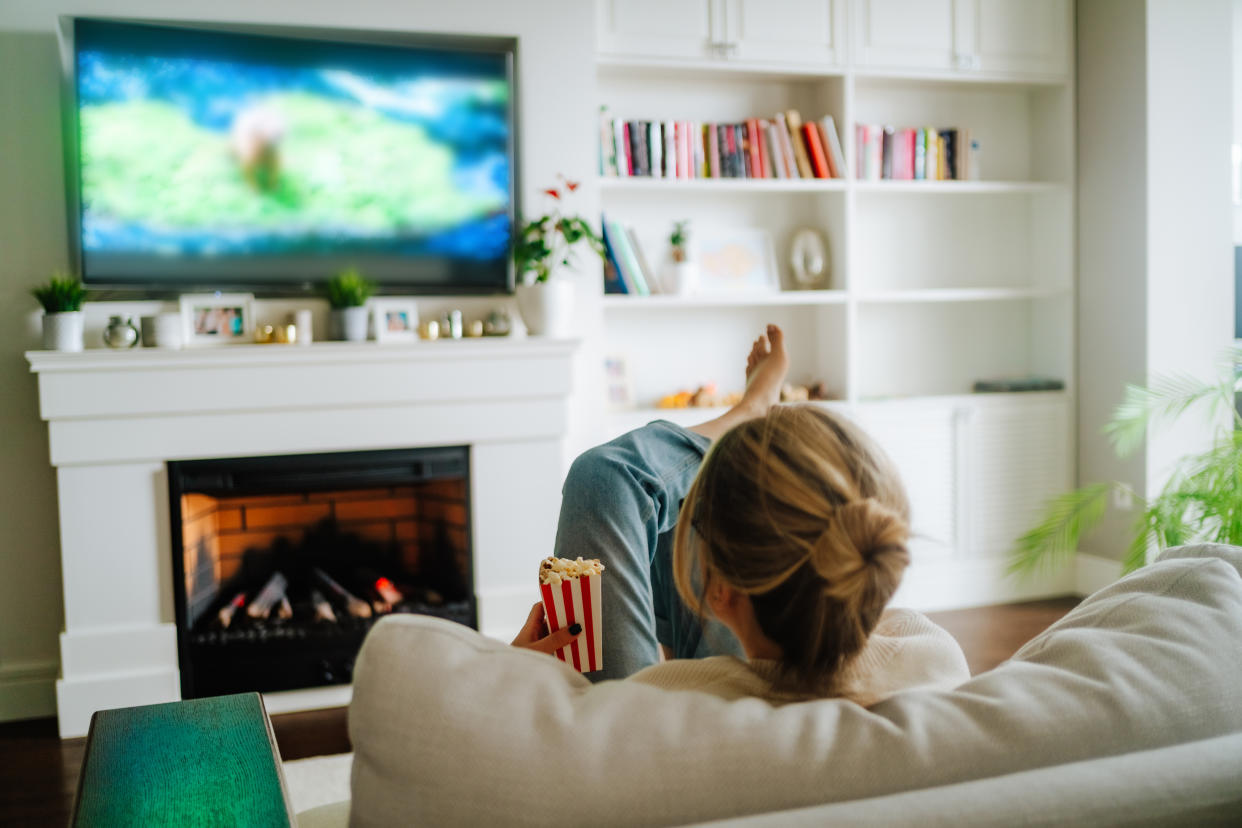 Blond woman with hair bun watching TV on a cozy sofa against fireplace indoors