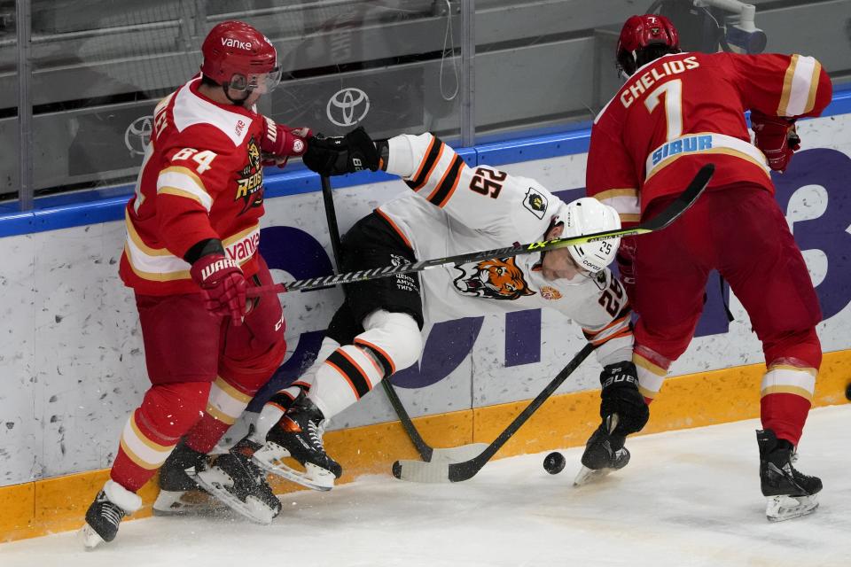 Kunlun Red Star's Victor Bartley, left, sends Amur's Radan Lenc, center, down during the Kontinental Hockey League ice hockey match between Kunlun Red Star Beijing and Amur Khabarovsk in Mytishchi, just outside Moscow, Russia, Monday, Nov. 15, 2021. Many of Kunlun Red Star's players are aiming to represent the Chinese national team at the Olympics in Beijing. (AP Photo/Alexander Zemlianichenko)