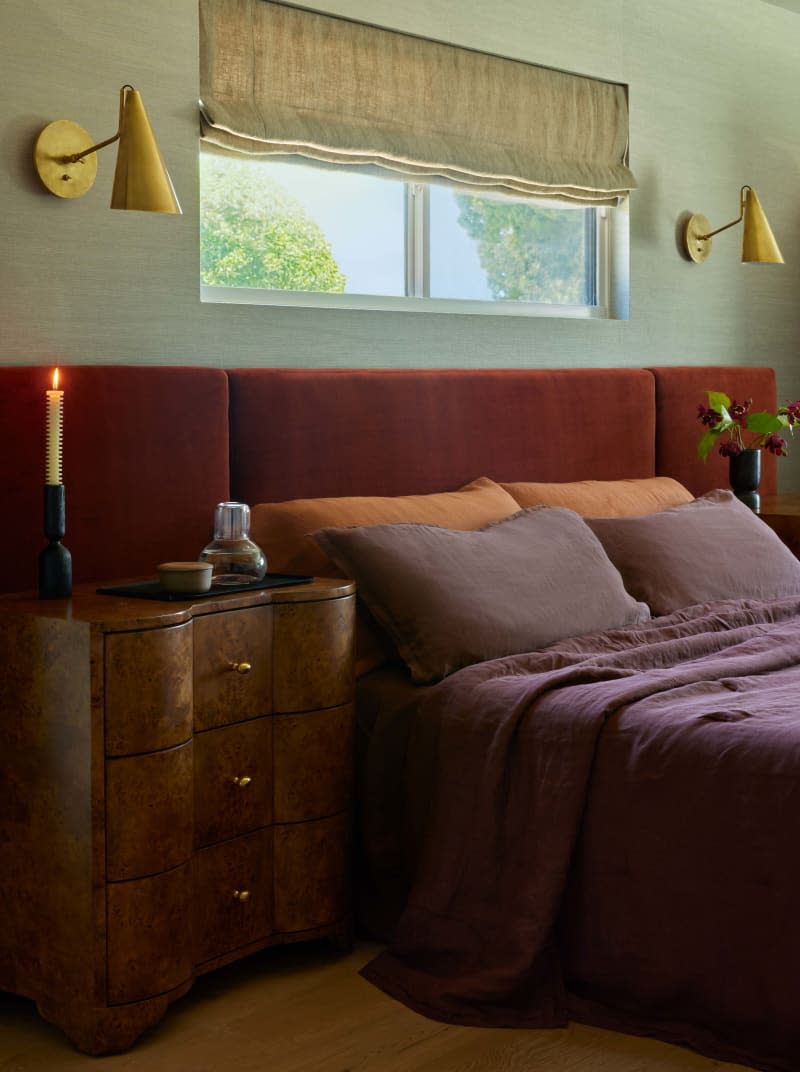 Light sage green wall, maroon bedding, maroon long wall mounted headboard, vintage wood curved night stand