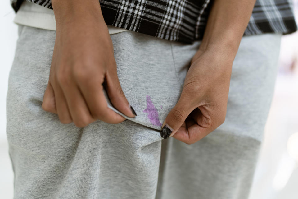 Close-up of a person's hands adjusting their gray sweatpants with a subtle purple and pink stain