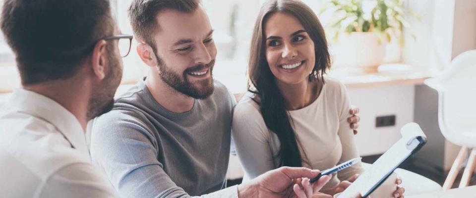 Smiling couple sit in office, prepare to sign papers as man hands over pen.