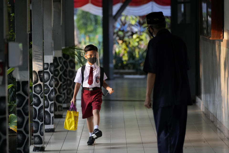 Staff greets a student during the first day of school reopening at an elementary school in Jakarta, Indonesia, Monday, Aug. 30, 2021. Authorities in Indonesia's capital kicked off the school reopening after over a year of remote learning on Monday as the daily count of new COVID-19 cases continues to decline. (AP Photo/Dita Alangkara)