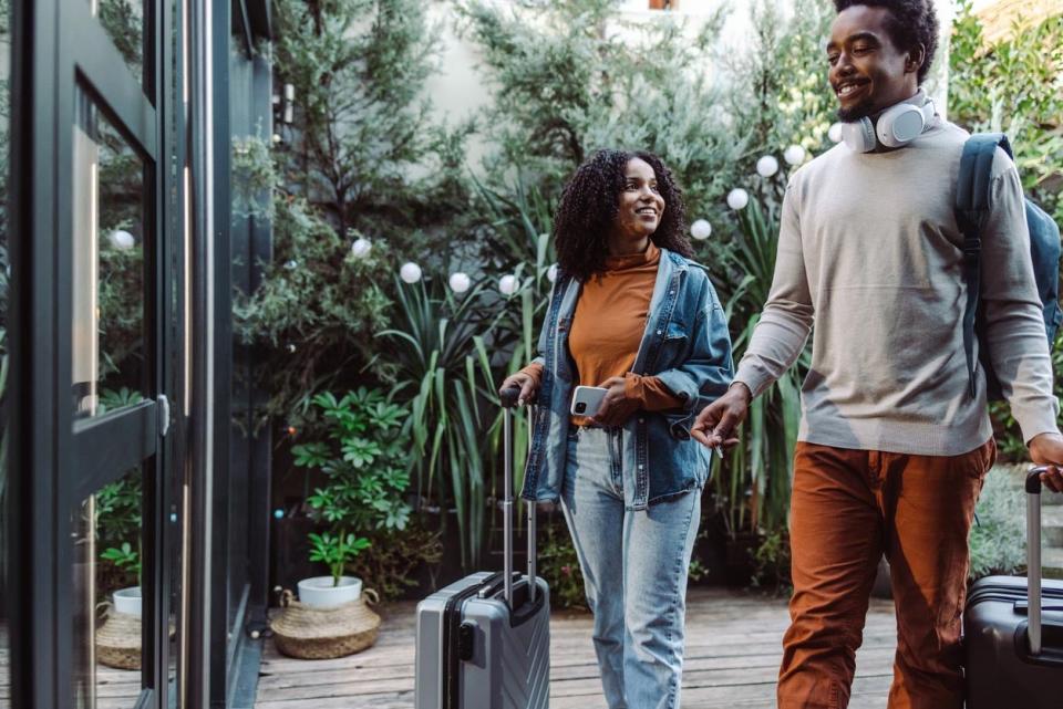 A man and a woman with suitcases walk towards a door.