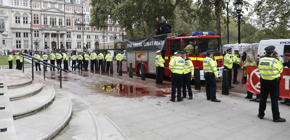 Extinction Rebellion climate activists stand on a fire engine outside the Treasury building in London, Thursday, Oct. 3, 2019. Climate activists sprayed hundreds of liters (gallons) of fake blood on the British government building, hoping to underscore the damage humans are causing to the planet. (AP Photo/Alastair Grant)