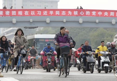 People ride past a pedestrian bridge with a banner reading "Unite closely around the Party Central Committee with Comrade Xi Jinping as the core" in Beijing, as the capital prepares for the 19th National Congress of the Communist Party of China, October 15, 2017. REUTERS/Jason Lee