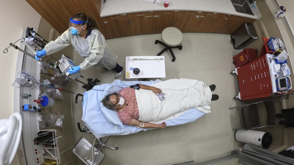 Angie Cleary, a registered nurse, cares for Joyce Johnson-Albert as she receives an antibody infusion while lying on a bed in a trauma room at the Upper Tanana Health Center Wednesday, Sept. 22, 2021, in Tok, Alaska. Johnson-Albert was optimistic but also realistic. "I just hope the next few days I'll be getting a little better than now," Johnson-Albert told a reporter on the other side of a closed, sliding glass door to the treatment room two days after testing positive for COVID-19 and while receiving an antibody infusion. "It's just hard to say. You can go either way." (AP Photo/Rick Bowmer)