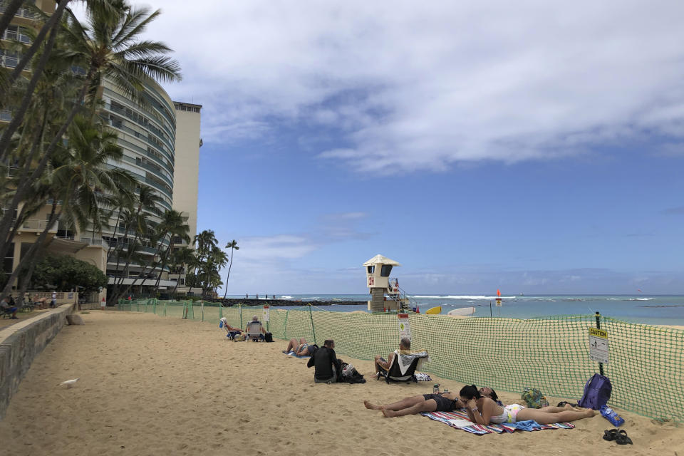 People sit behind a fenced off area of Kaimana Beach where a Hawaiian monk seal gave birth this week in Honolulu, Thursday, April 20, 2023. Officials fenced off a large stretch of a popular Waikiki beach to protect the seal and her days-old pup. The unusual move highlights the challenges of protecting endangered species in a state that attracts millions of travelers every year. (AP Photo/Audrey McAvoy)