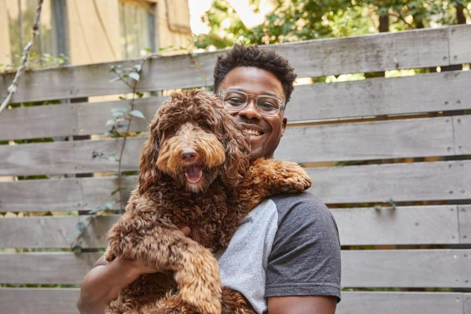 Young man holds fluffy copper-colored dog outside