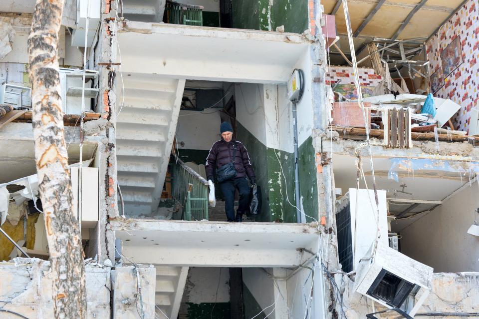 A man carries belongings out of a heavily damaged apartment building 