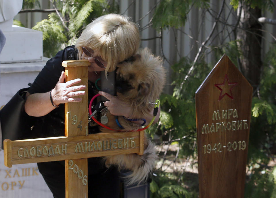 A woman with dog kisses the wooden cross atop the former strongman Slobodan Milosevic grave during funeral of his wife Mirjana Markovic, marker on right, at the yard of his estate in his home town of Pozarevac, Serbia, Saturday, April 20, 2019. Markovic died last week in Russia where she had been granted asylum. The ex-Serbian first lady had fled there in 2003 after Milosevic was ousted from power in a popular revolt and handed over to the tribunal in The Hague, Netherlands. (AP Photo/Darko Vojinovic)