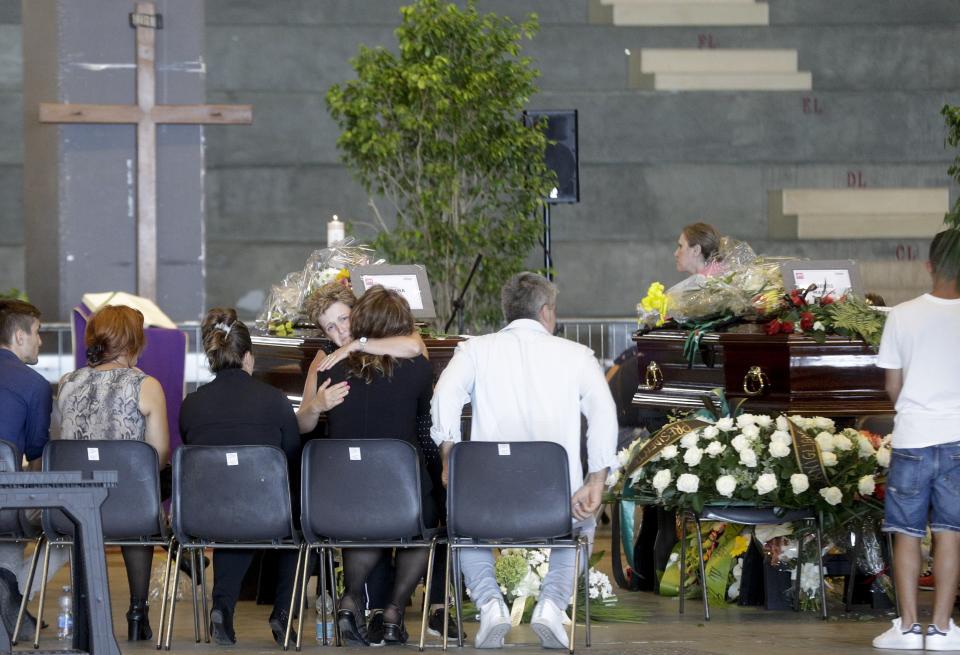 Mourners sit by the coffins of some of the victims of the Morandi highway bridge collapse, in Genoa, Italy, Friday, Aug. 17, 2018. Officials say 38 people are confirmed killed and 15 injured. Prosecutors say 10 to 20 people might be unaccounted-for and the death toll is expected to rise. (AP Photo/Gregorio Borgia)