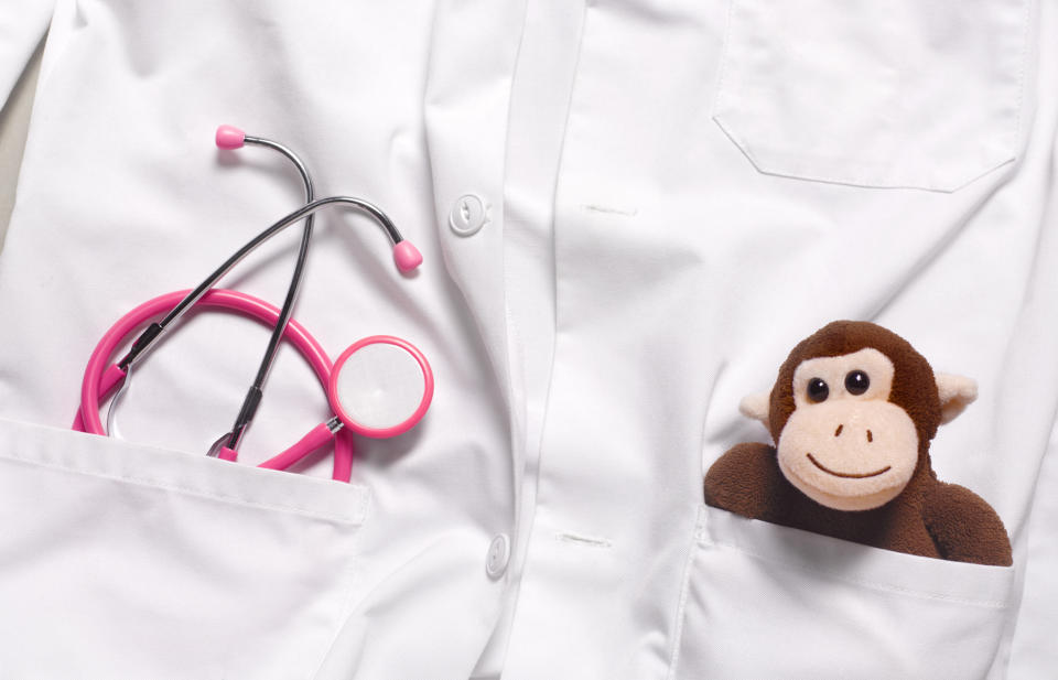 Close-up of a medical professional's white coat with a stethoscope and a plush monkey in the pocket, suggesting pediatric care