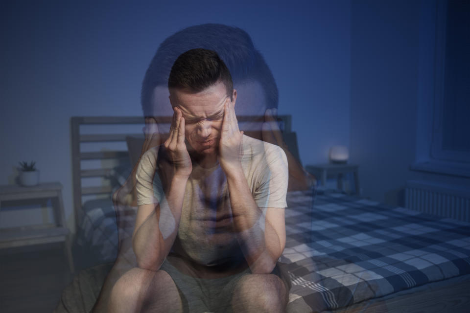 Anxious man with headache sitting in bedroom with head in hands.