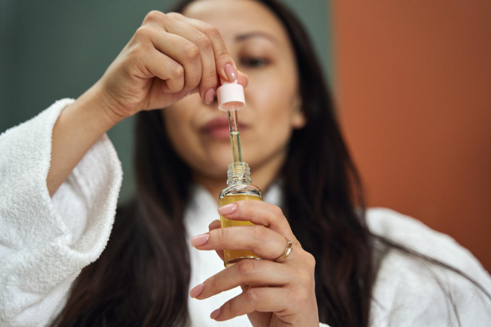 A girl holding a bottle of oil and picking up its dropper