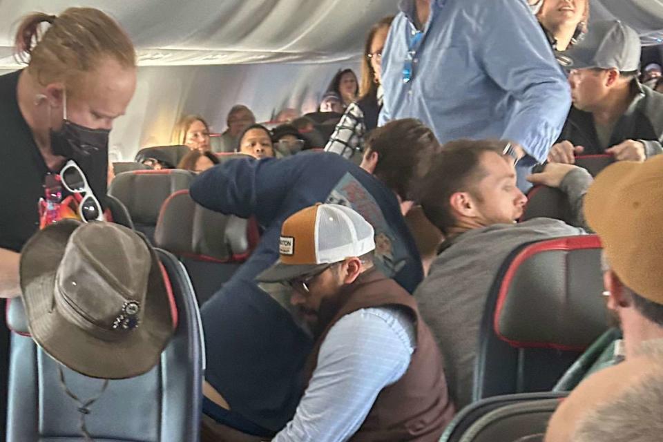 <p>DonnieDoesWorld/X</p> Passengers restrain the man after he tried to open the emergency exit door. 