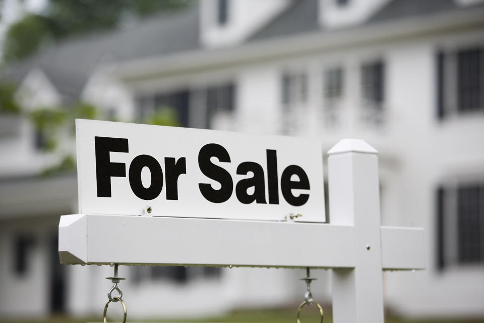A "For Sale" sign in front of a large house