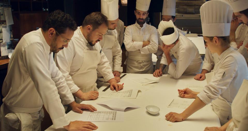 Restaurant workers gather around a table wearing white in "Menus-Plaisirs – Les Troisgros."