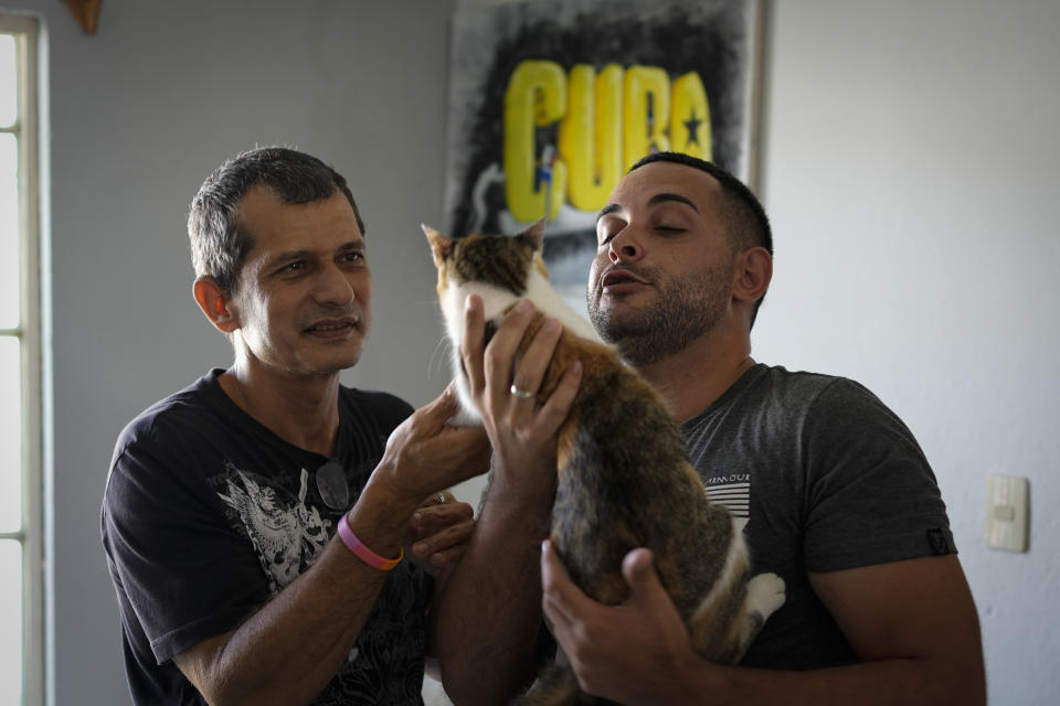 Partners Lázaro “Lachi” González, left, and Adiel González play with their cat Zaida, on the sidelines of an interview at their home in Matanzas, Cuba, Thursday, Oct. 7, 2021. The socialist government recently published a draft Family Law and asked for public comment ahead of a referendum on legalizing same-sex marriage, as well as expanding grandparents rights, allowing for prenuptial agreements and in cases of divorce, create financial consequences for those who have committed gender violence, amid a total of 480 articles. (AP Photo/Ramon Espinosa)