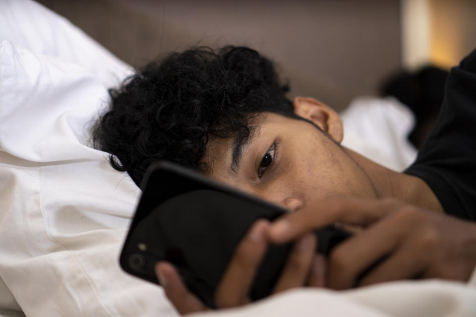 A person lies in bed, holding and looking at a smartphone closely