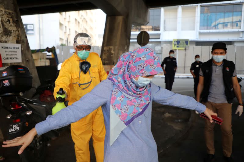 FILE PHOTO: A worker sprays disinfectant on a woman during the movement control order due to the outbreak of the coronavirus disease (COVID-19), in Kuala Lumpur