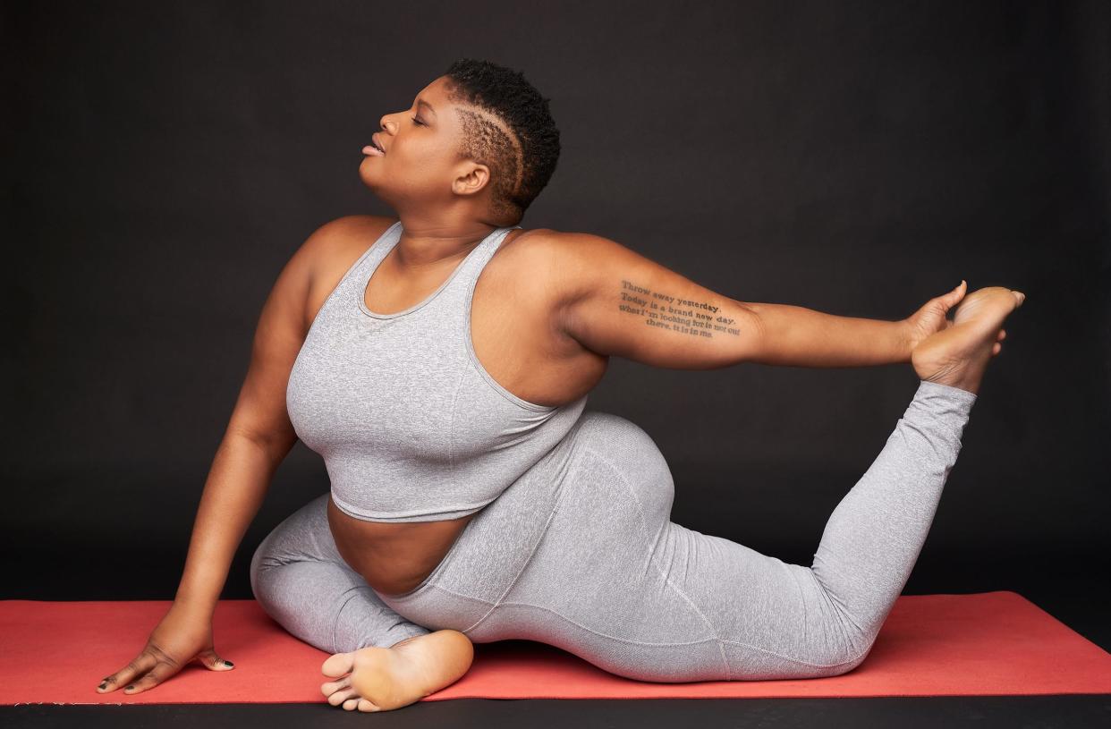 Jessamyn Stanley does a yoga pose while wearing a gray two-piece matching exercise set on a light red mat.