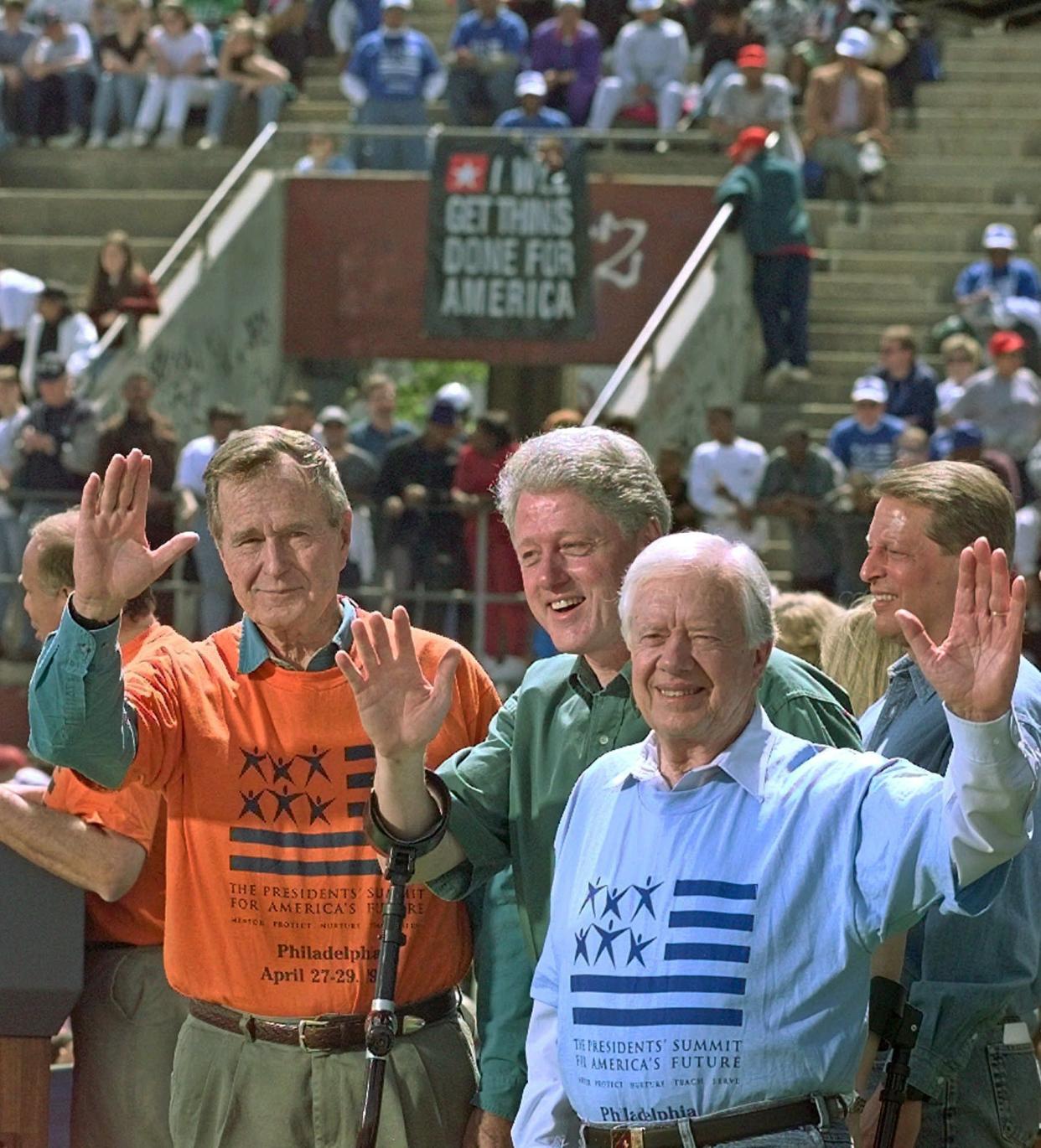 Former Presidents George H. W. Bush, left, and Jimmy Carter, right, stand with President Bill Clinton and wave to volunteers during a kick-off rally for the President Clinton's Volunteer Summit at Marcus Foster Stadium on April 27, 1997, in Philadelphia. Vice President Al Gore stands at rear.