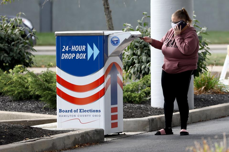 A voter drops off her ballot in the drop box as motorists queue to enter the Hamilton County Board of Elections to either vote in person or drop off their completed absentee ballots, Friday, Oct. 9, 2020, in Norwood, Ohio. 