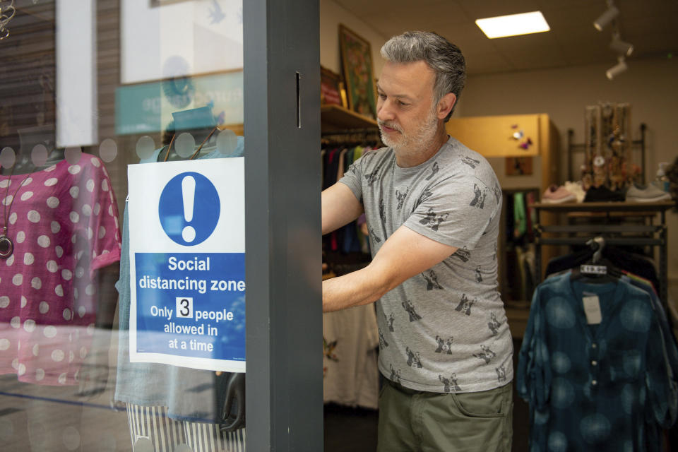 Retailer Clive Williams installs a sign in the window of his Pop Up Clothing Company store, in Stratford-upon-Avon, Warwickshire, England, Sunday, June 14, 2020. Lockdown restrictions are slowly being eased, which should see the economy start to pick up. On Monday, nonessential shops, such as department stores and electronic retailers, can reopen if they can abide by social distancing requirements. (Jacob King/PA via AP)