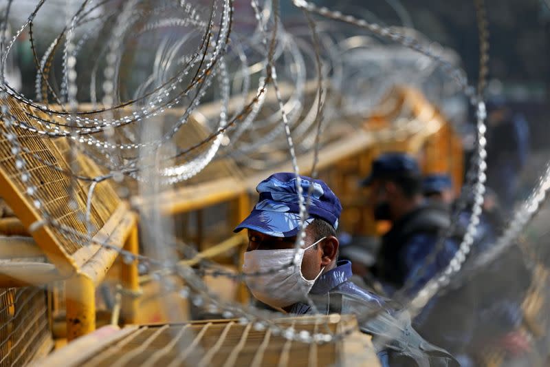 A member of the Rapid Action Force (RAF), wearing a protective face mask, is seen through barbed wire at the site of a protest against the newly passed farm bills at Singhu border near Delhi