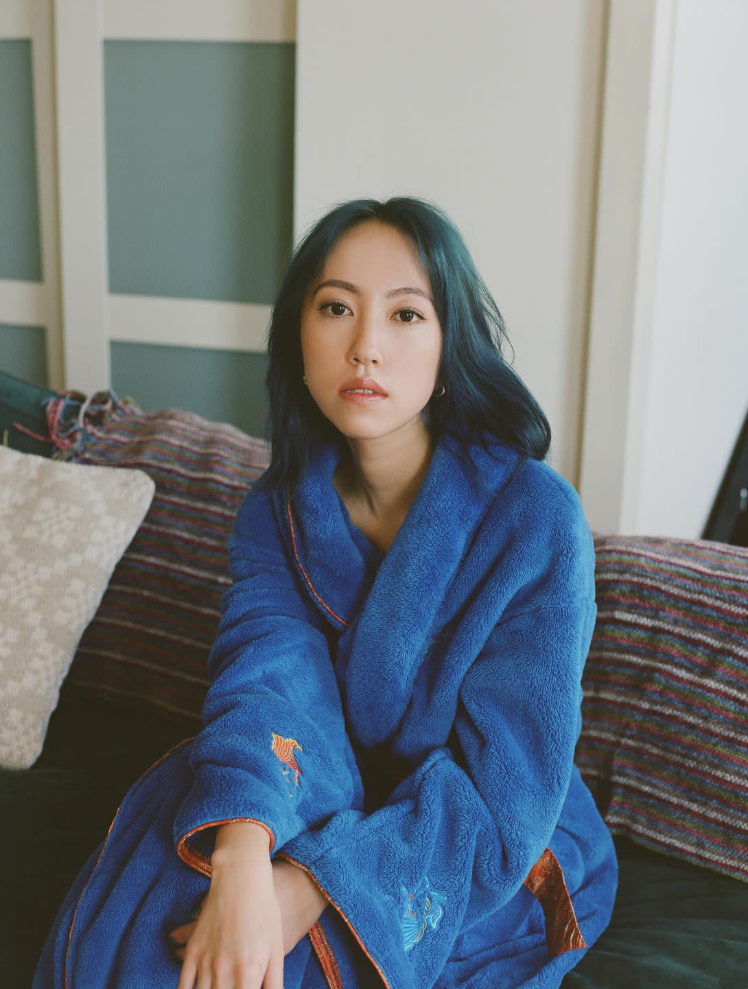 designer daisy wang of dawang sits on a couch in a blue bathrobe