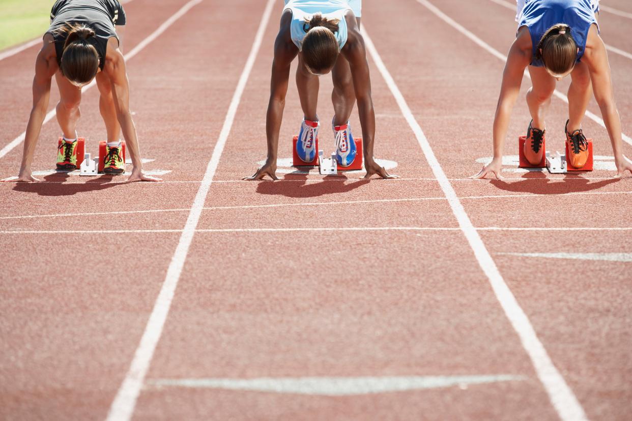 Three women runners crouched down at the starting block.