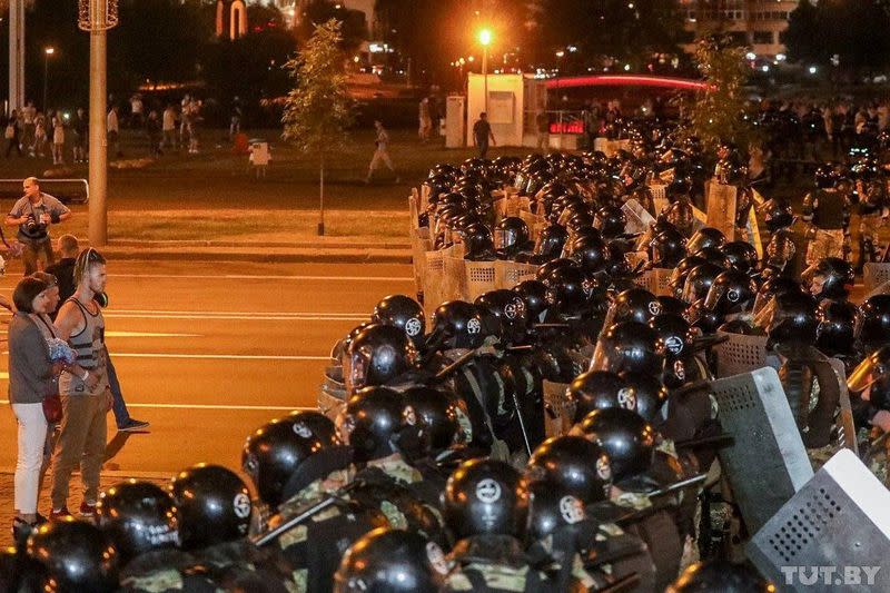 Opposition supporters stay in front of law enforcement officers blocking a street after poll closed at presidential election in Minsk