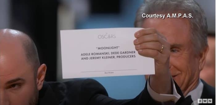 A man holds a piece of paper with "Moonlight" written on it up to the camera, looking serious