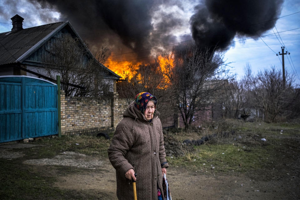 An elderly woman stands near a burning building following shelling (Sergey Shestak / AFP via Getty Images)