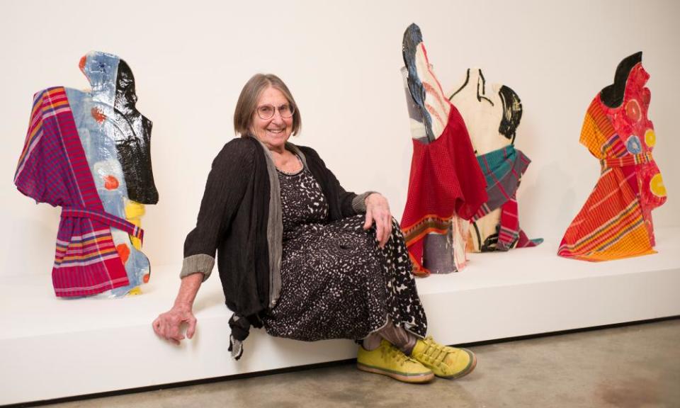 A smiling woman with yellow shoes sits in front of colourful ceramic figures