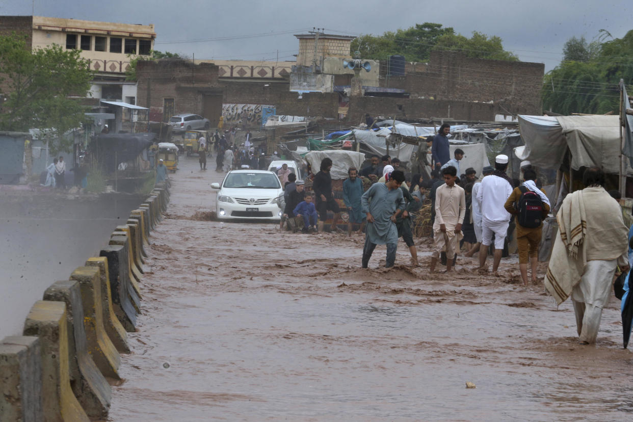 People wade through a flooded bridge on a stream, which is overflowing following heavy rains, on the outskirts of Peshawar, Pakistan, Monday, April 15, 2024.  / Credit: Muhammad Sajjad / AP