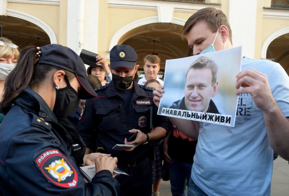 Police officers check documents of a man standing with a placard with an image of Alexei Navalny during a gathering to express support for the opposition leader after he was rushed to intensive care in Siberia suffering from a a suspected poisoning, in St. Petersburg on August 20, 2020.<span class="copyright">Olga Maltseva—AFP/Getty Images</span>