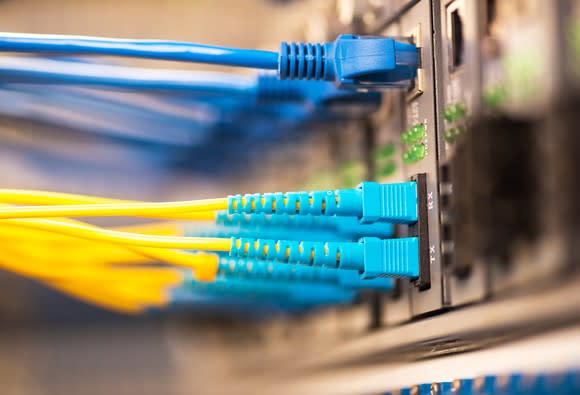 Several sets of colorful Ethernet and fiber-optic network cables plugged into a rack of optoelectronic transceiver modules.