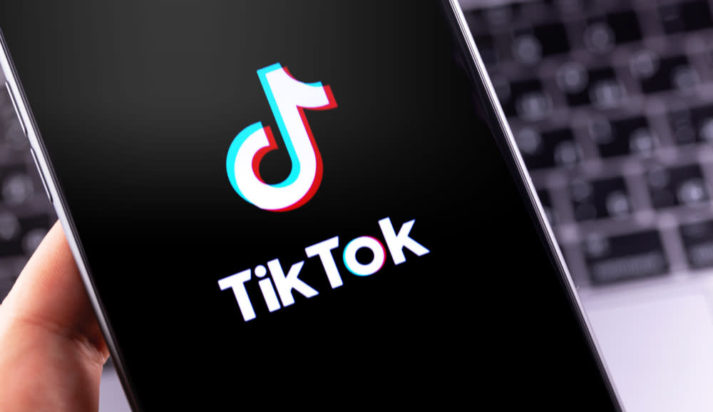  The TikTok logo displayed on a smartphone screen with a computer keyboard in the background. 