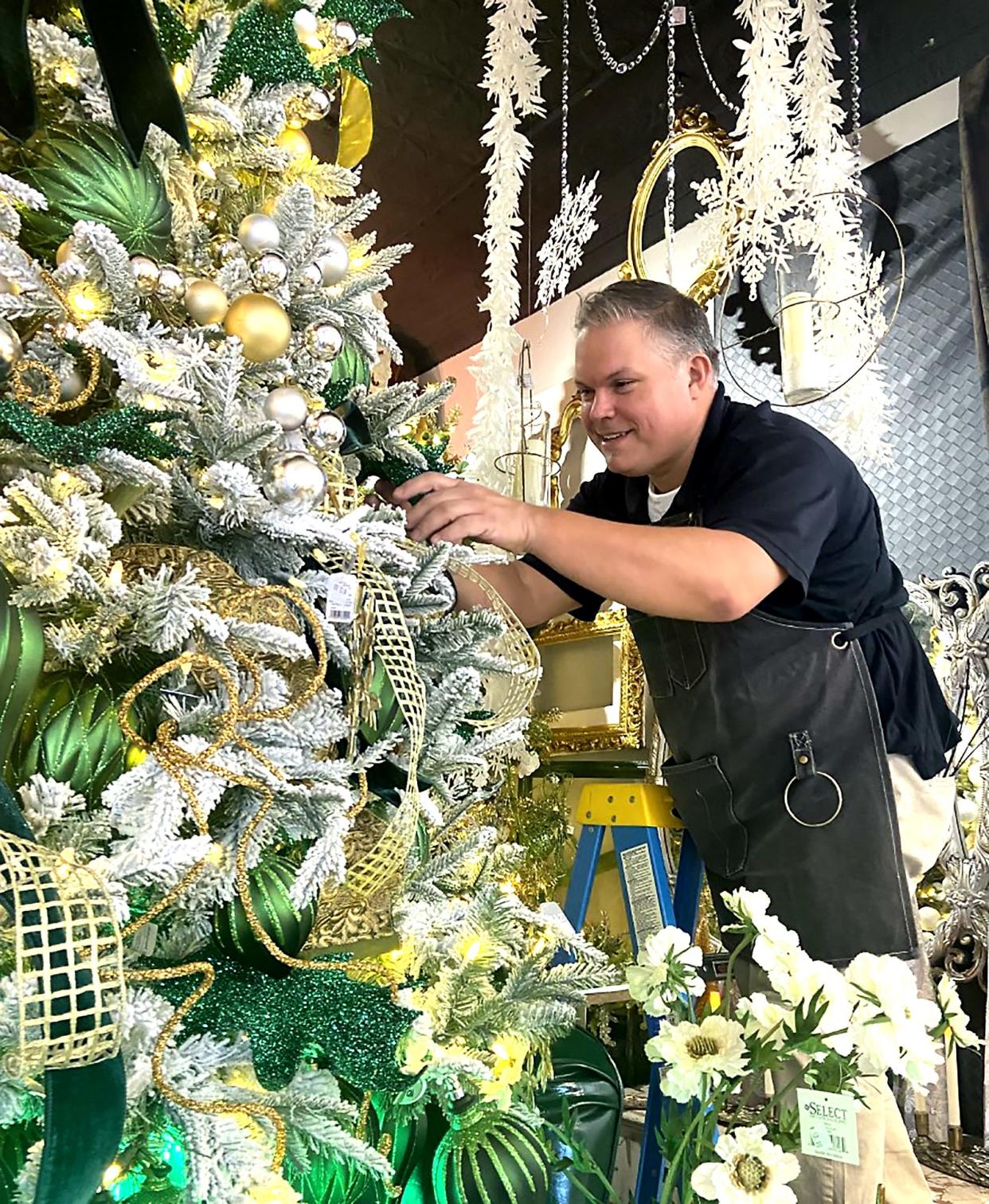 Doug Bates works on an emerald green, gold and white tree inside Designs by Vogt's. He had always wanted to decorate a tree in the colors, he said.