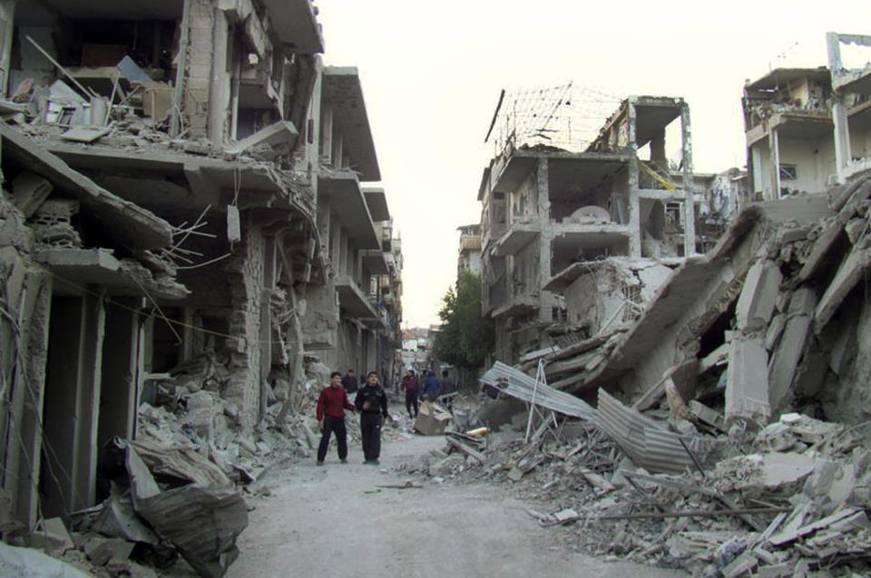 FILE - In this file photo released on Thursday, Nov. 29, 2012 by the anti-government activist group Homs City Union of The Syrian Revolution, which has been authenticated based on its contents and other AP reporting, Syrian citizens walk in a destroyed street that was attacked by Syrian warplanes, at Abu al–Hol street in Homs province, Syria. Exhausted and worn out from a year-long siege, hundreds of Syrian rebels on Wednesday, May 7, 2014, left their last remaining bastions in the heart of Homs under a ceasefire deal with government forces. (AP Photo/Homs City Union of The Syrian Revolution, File)